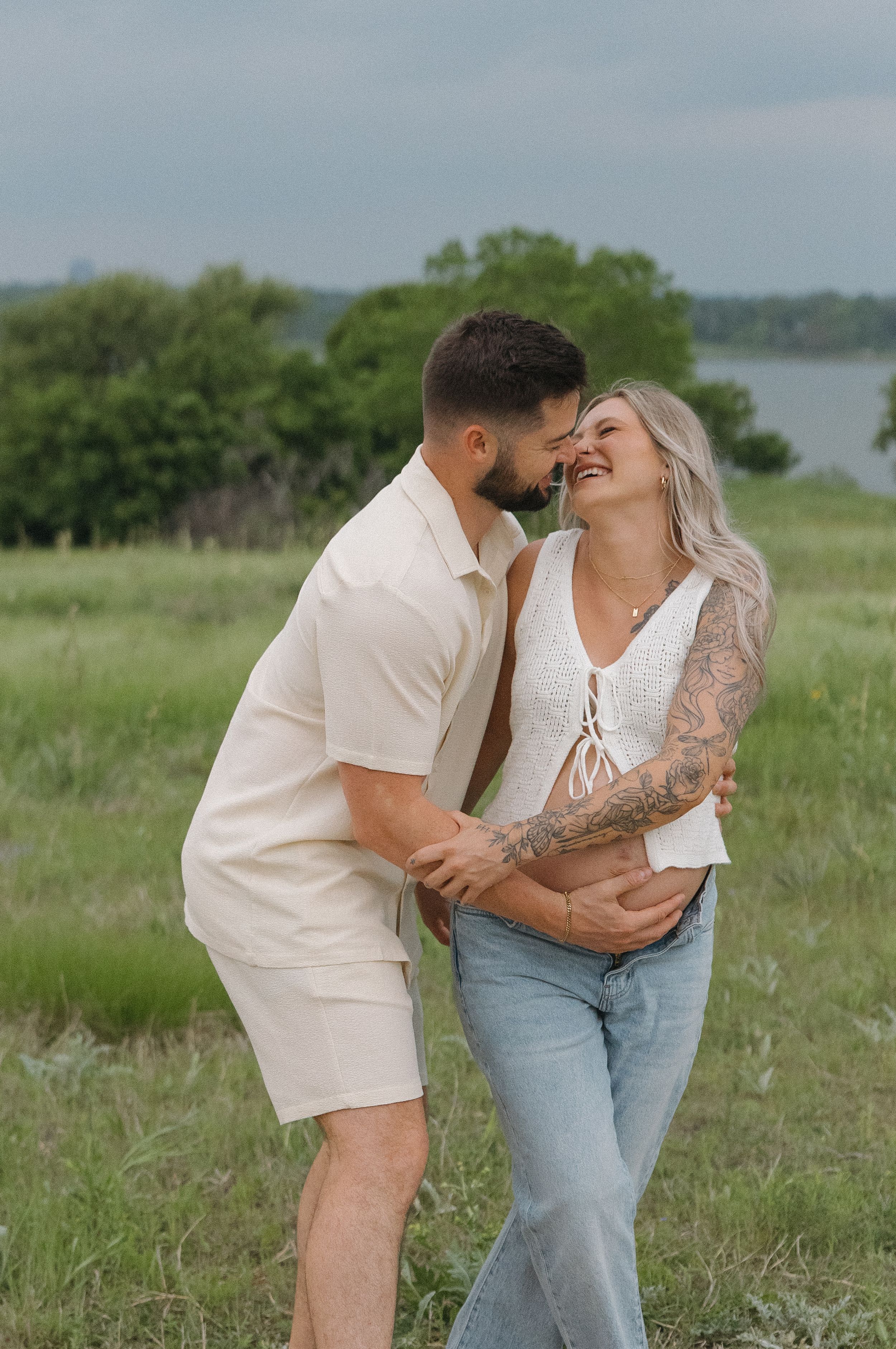 Couple laughing together in casual summer outfits against scenic natural backdrop.