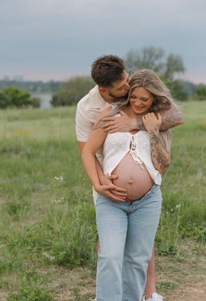 Expecting couple shares tender moment in grassy field during maternity photo shoot wearing casual attire.