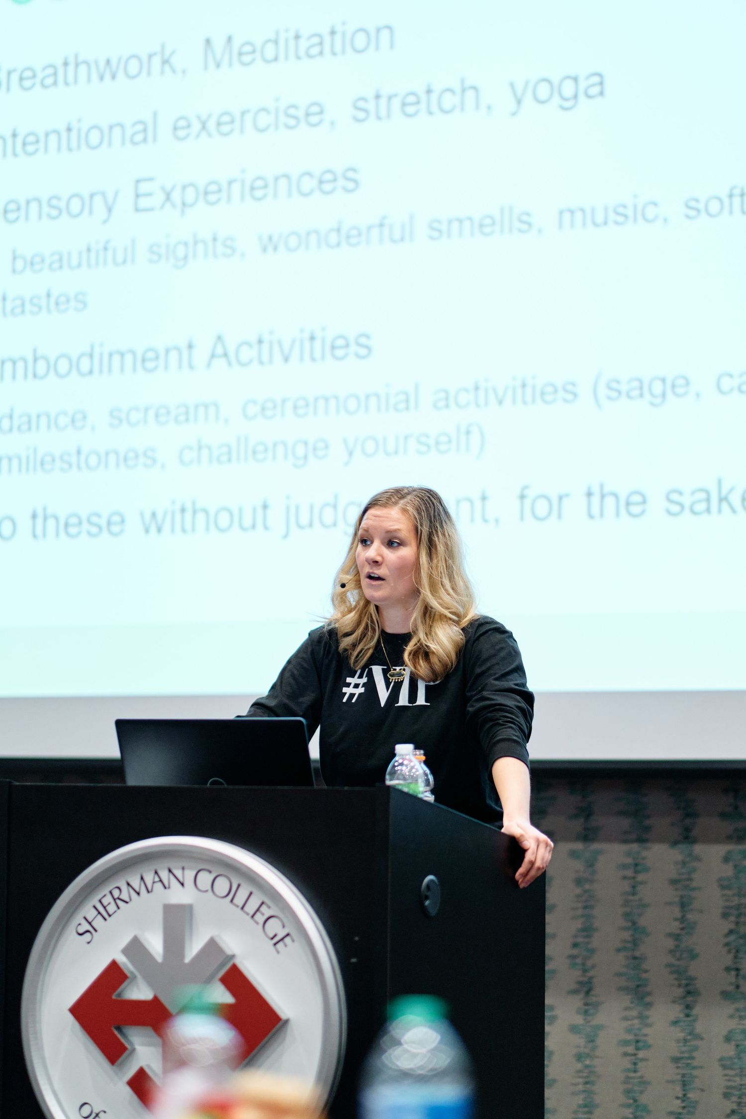 Speaker presents at podium with Sherman College logo during educational presentation on meditation and wellness topics.