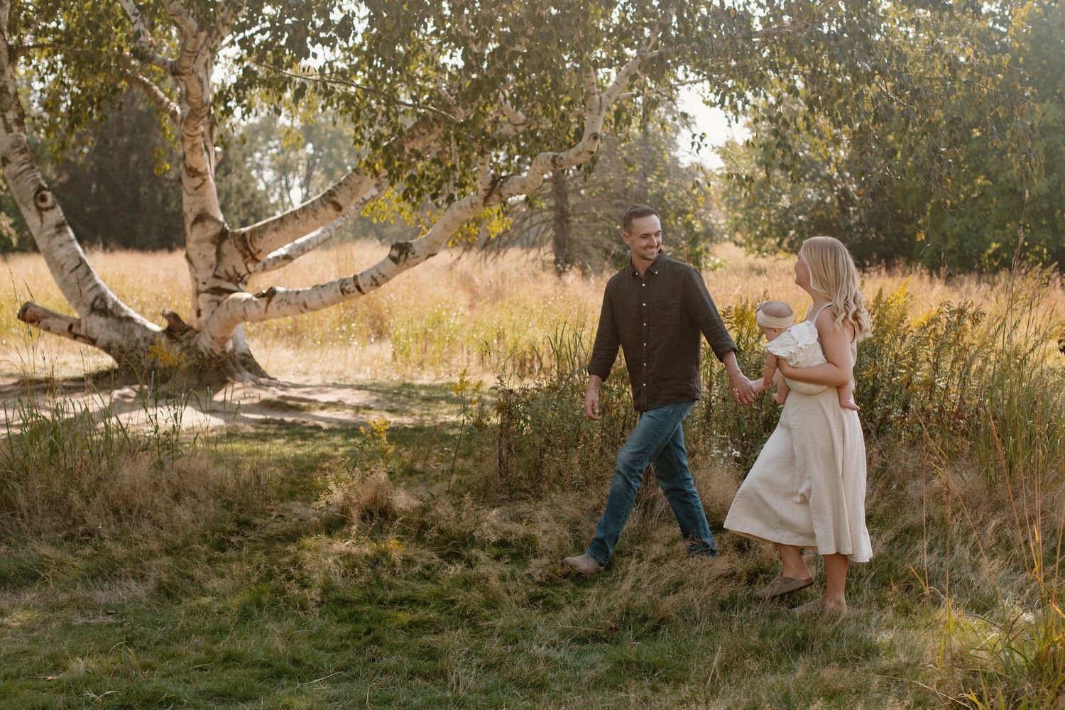 A family of three during their Grand Rapids family session walking through a field.