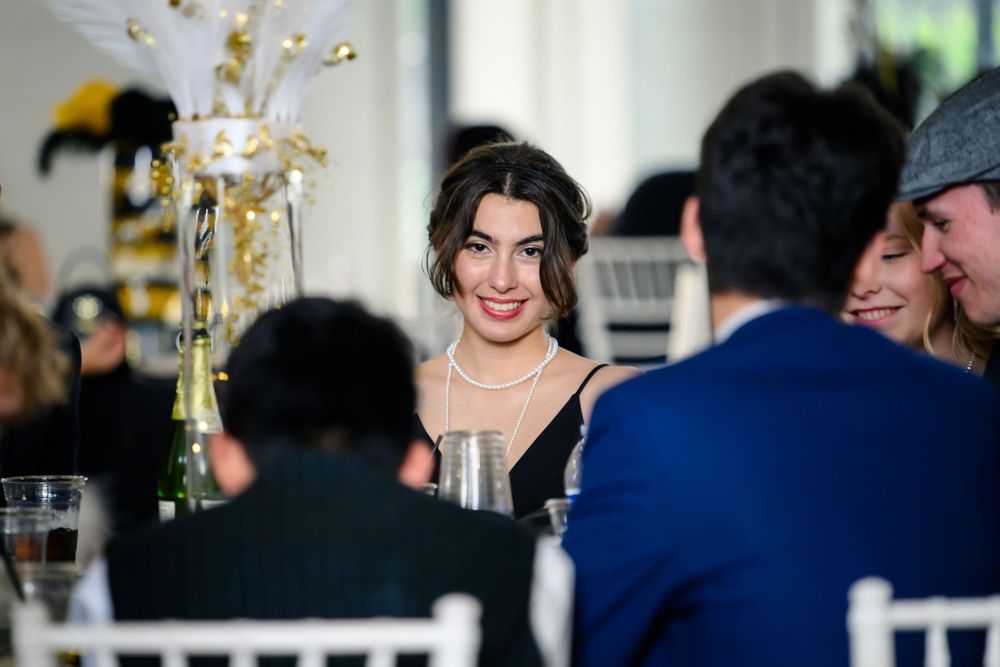 A candid moment captured at an elegant indoor reception with guests seated at tables with floral centerpieces.