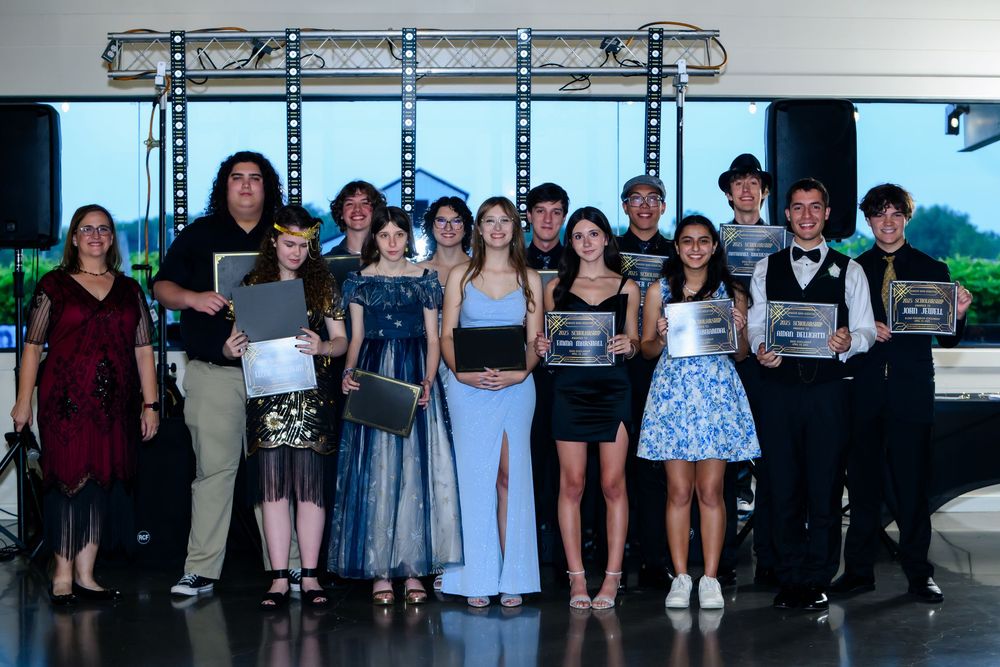 A group of performers stand together under stage lighting holding certificates during an awards ceremony.