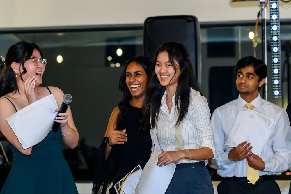 A joyful group of young people laugh together at an evening event indoors.