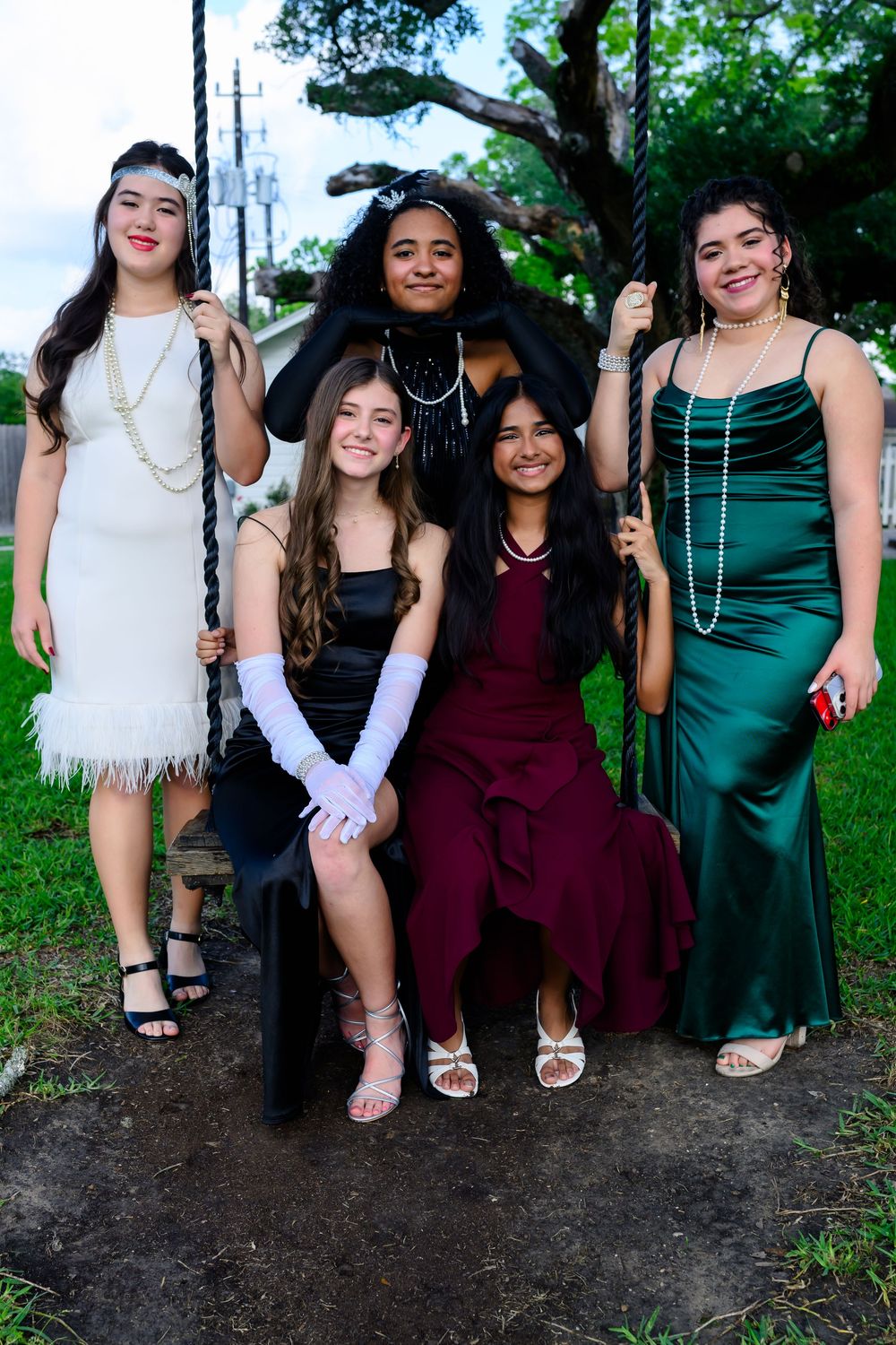 A group in formal attire poses together outdoors for a special event photo wearing elegant dresses in various colors.