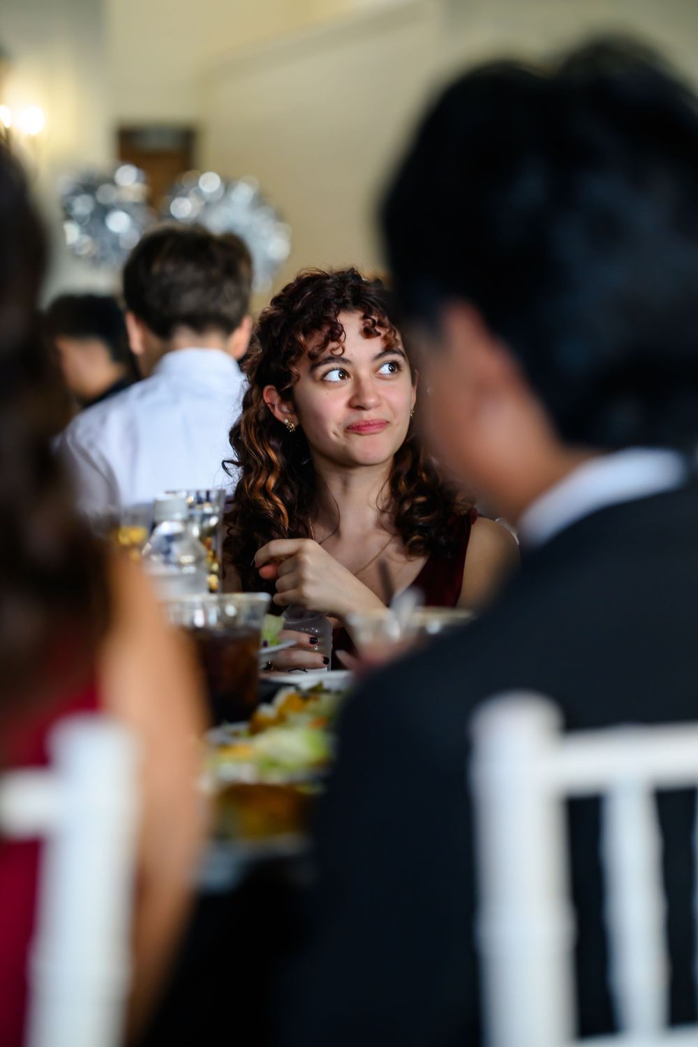 A guest with curly dark hair smiles warmly while enjoying conversation during an elegant dinner party.