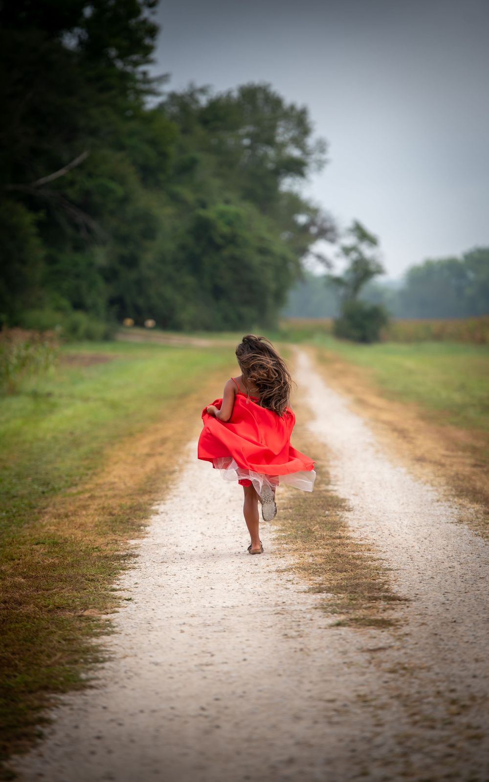 Figure in a flowing red dress running down a misty country road.