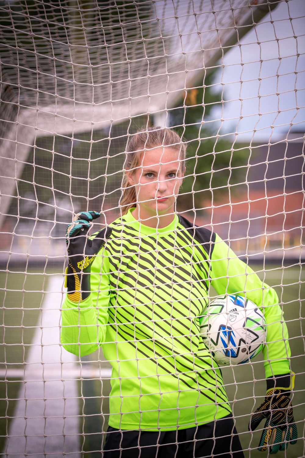 Soccer goalkeeper in neon yellow uniform holds ball in front of net.