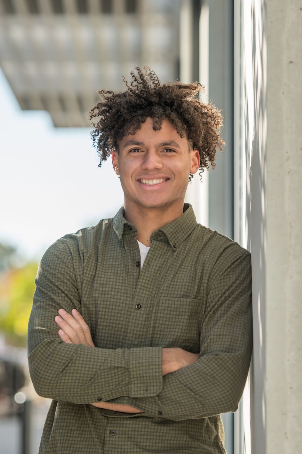 Professional portrait of someone in olive green shirt leaning against wall with natural lighting.