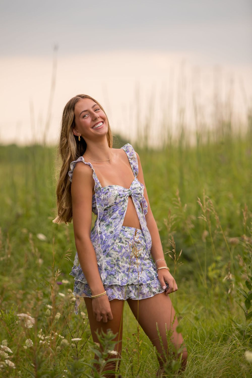 Someone wearing a floral summer dress poses joyfully in a sunlit meadow with tall grass.