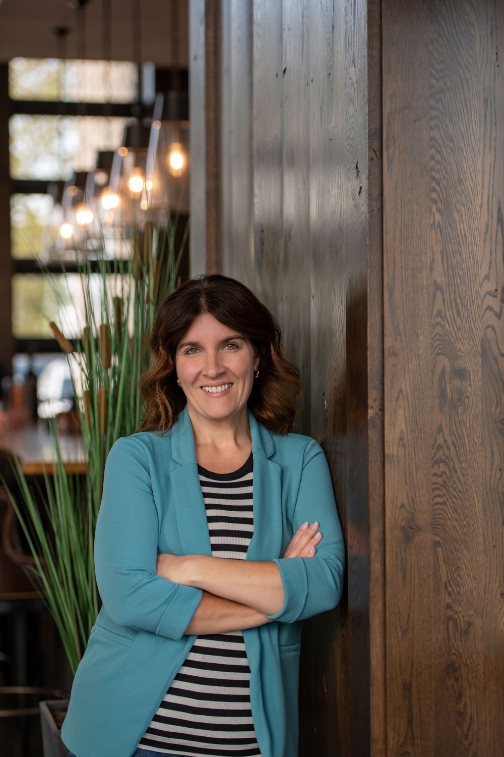 Professional portrait of someone in a teal blazer and striped shirt against a wooden wall.