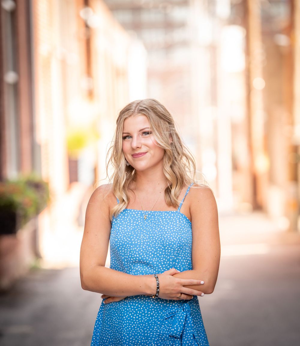 Portrait of woman in blue dress standing outdoors in urban setting.