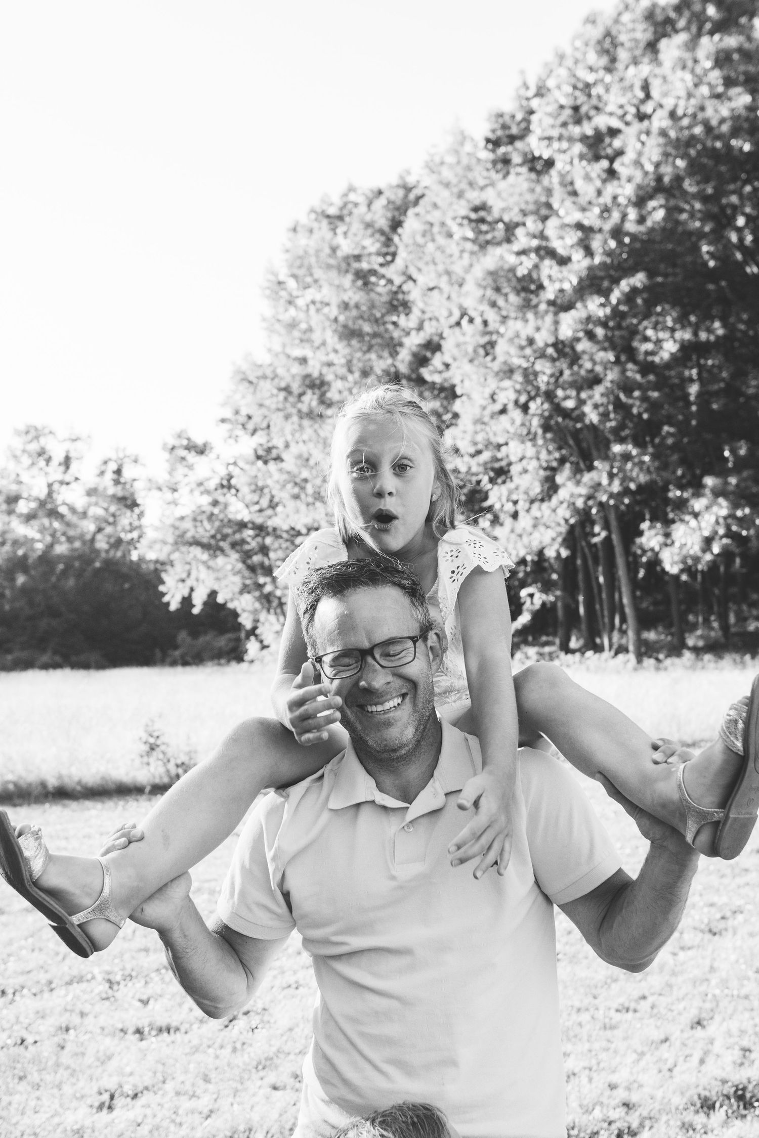 Black and white photo of a playful outdoor scene with piggyback ride in a sunny natural setting surrounded by trees.