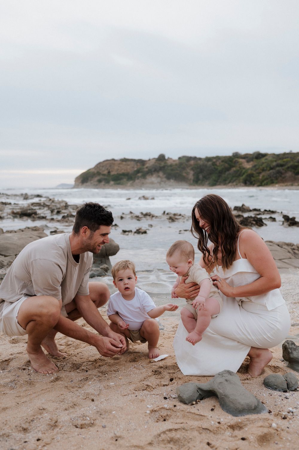 Family playing together on a rocky beach with coastal cliffs in background.