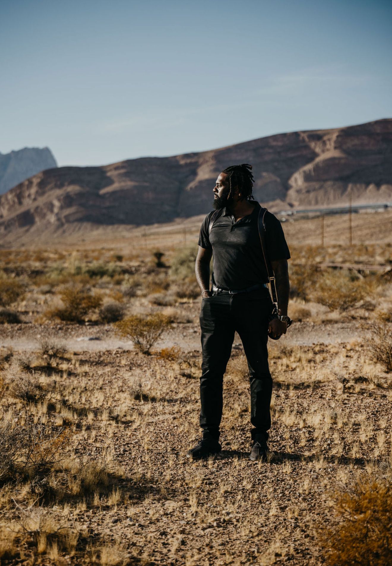 Silhouette of person in dark clothing standing against desert mountain backdrop.