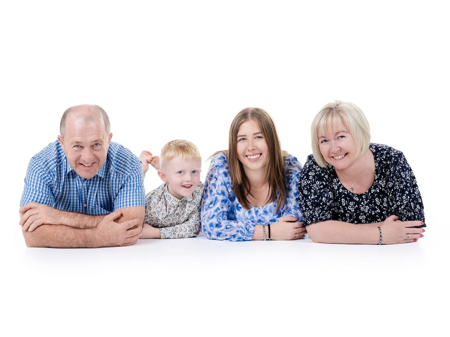 Multi-generational family members lying down in a row wearing casual clothing against white background.