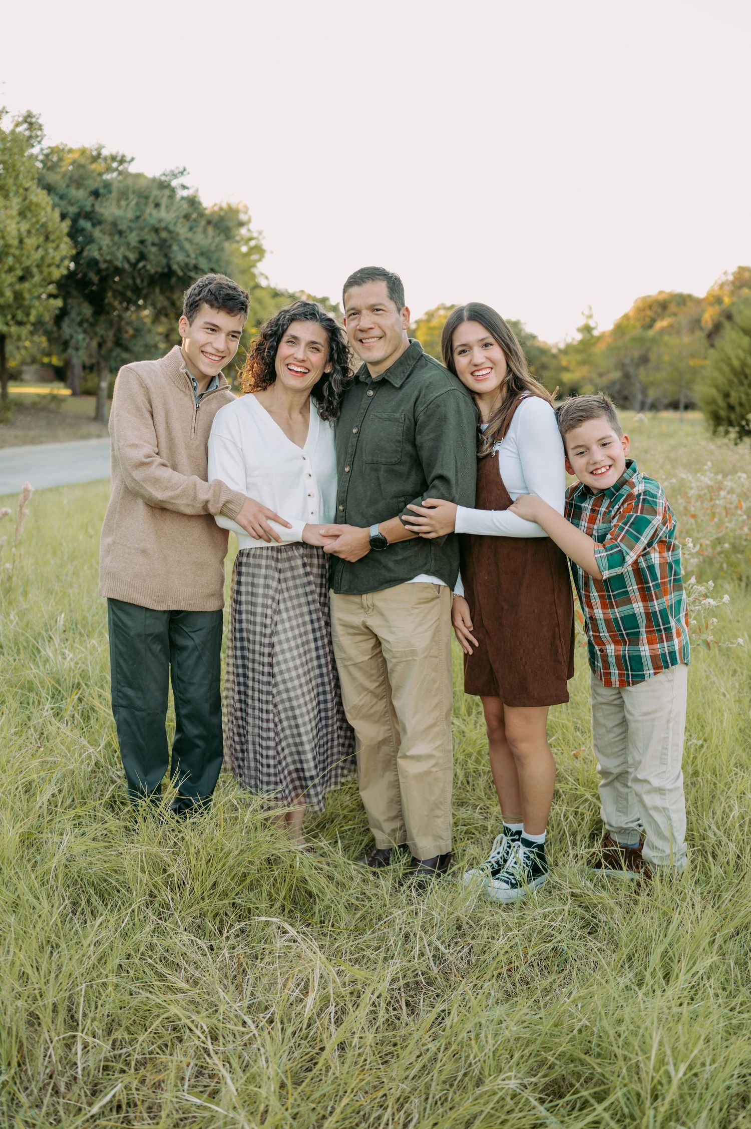 A family of five poses together outdoors in coordinated casual outfits.
