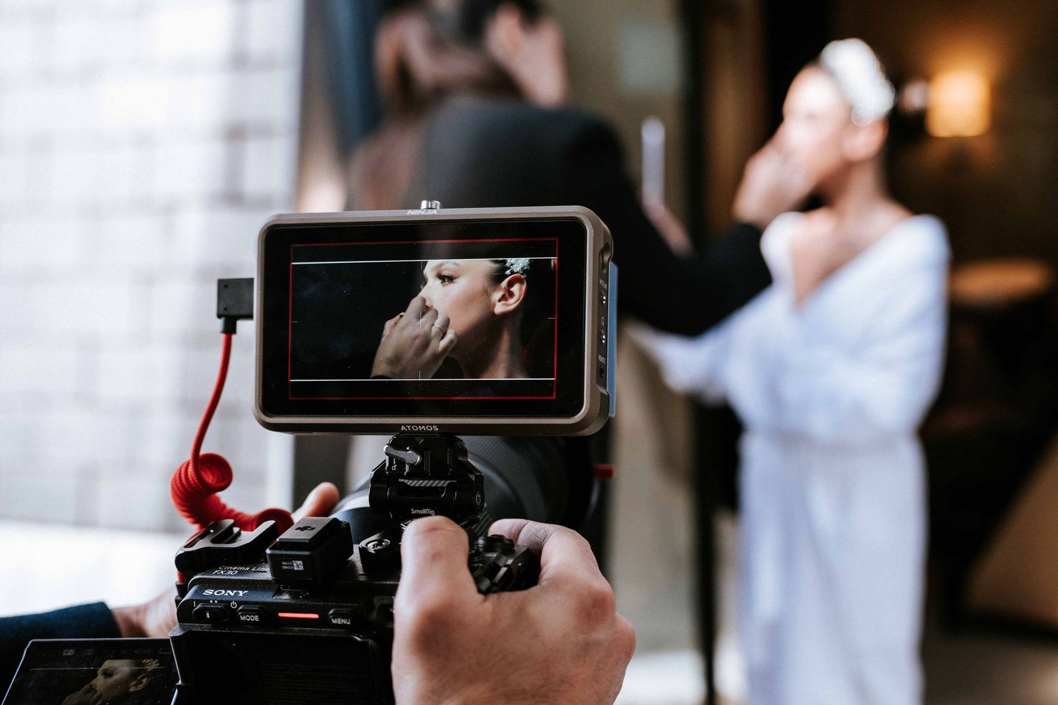 Video monitor display on professional camera showing behind-the-scenes filming of indoor scene.