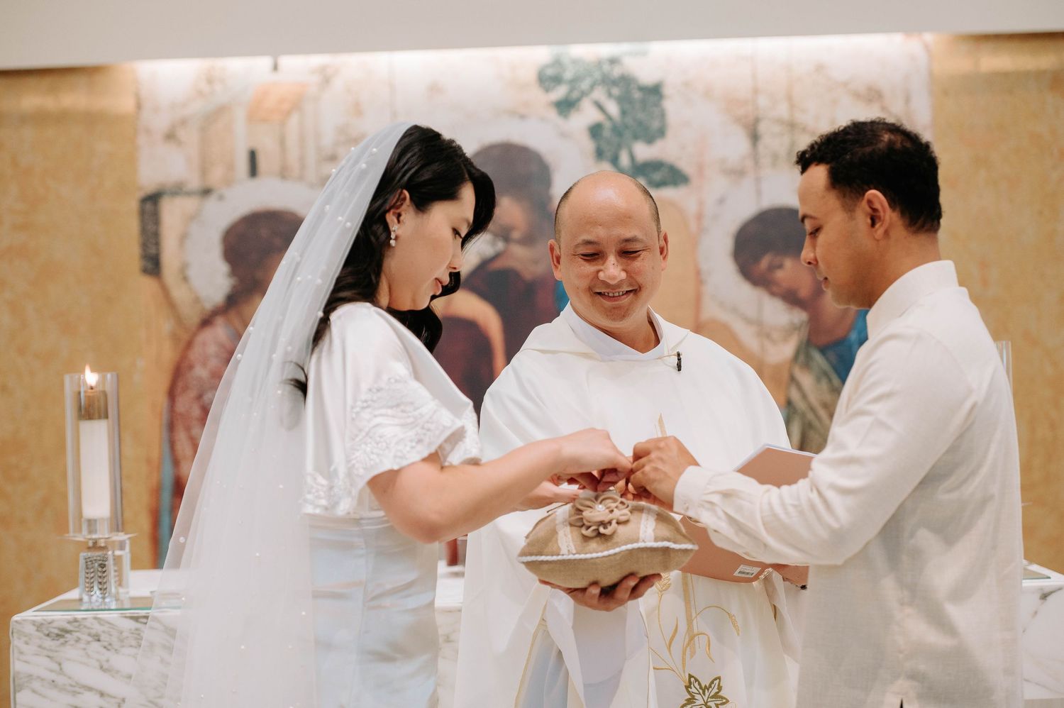 A couple exchanges rings during a traditional church wedding ceremony with an officiant presiding over the service.