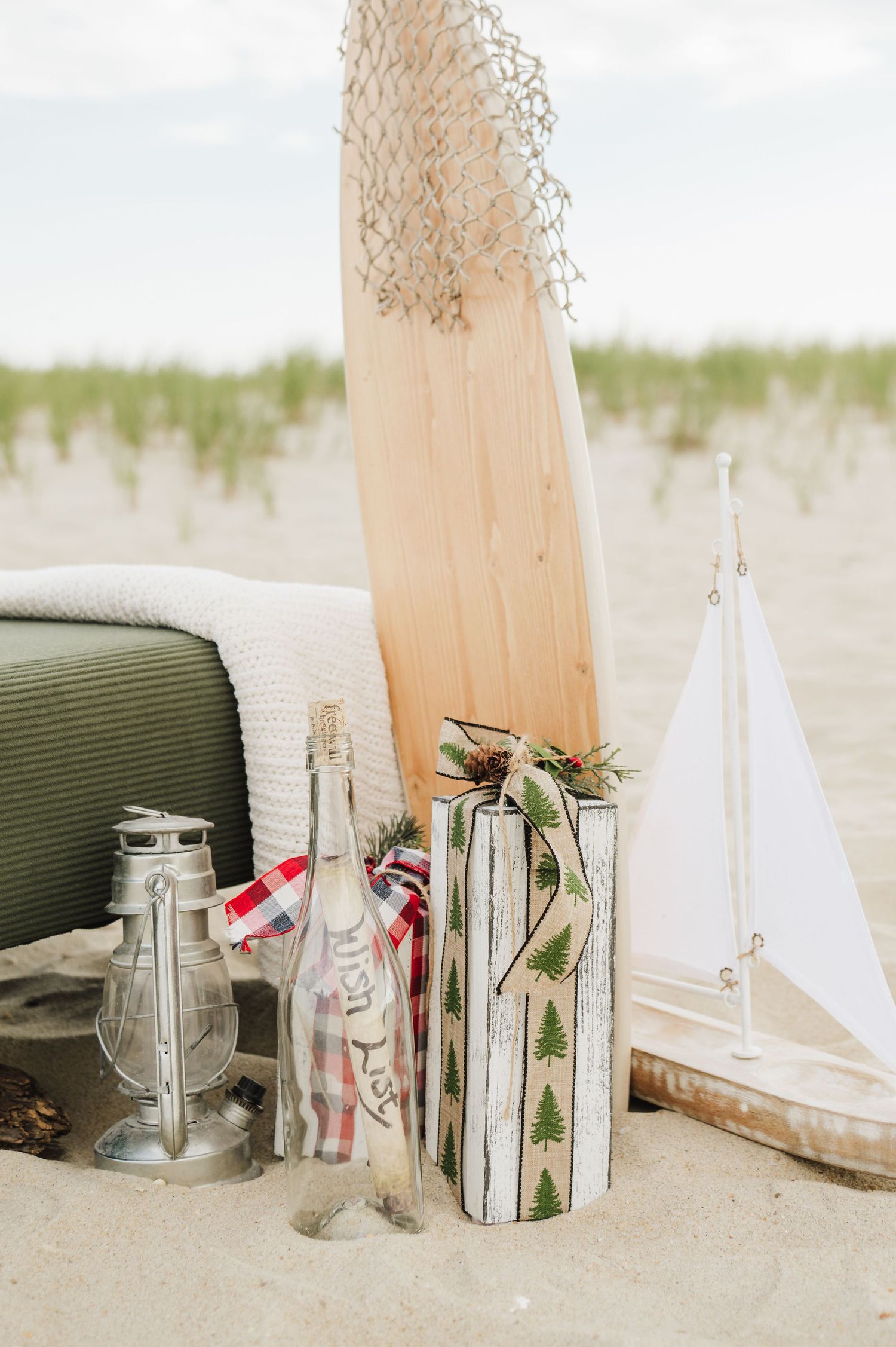 Nautical beach wedding decor with sailboat, lantern, message bottle, and wooden decorations on sandy shore.