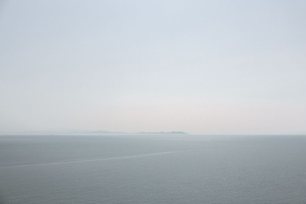 Minimalist seascape with soft grey sky meeting calm ocean at the horizon.