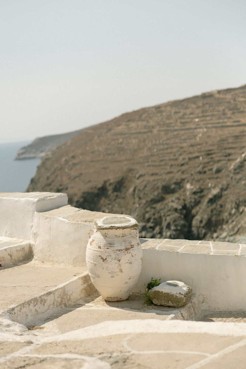 White ceramic pot rests on coastal terrace overlooking dramatic cliffside views of the Mediterranean.