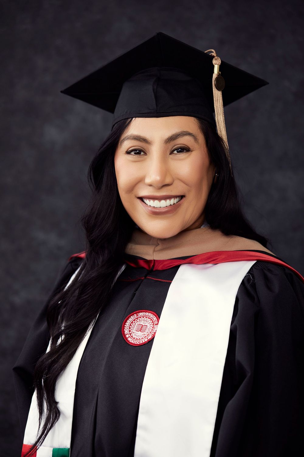Graduate in traditional black academic regalia with white stole smiles in professional portrait.