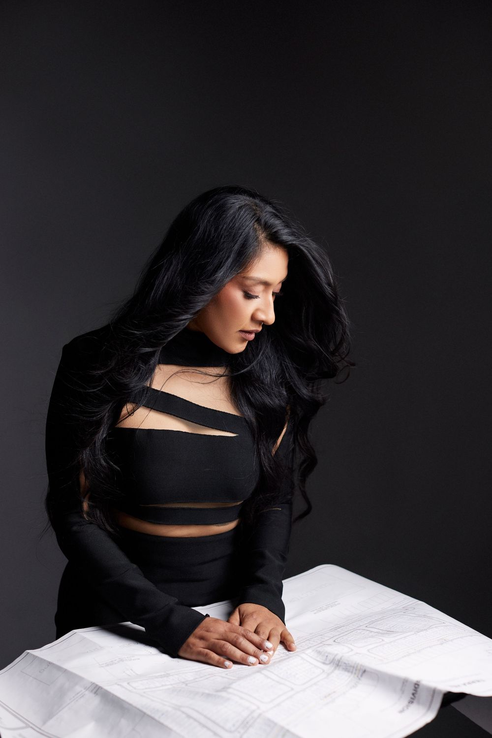 Woman in black outfit leans over white papers in dramatic studio lighting.
