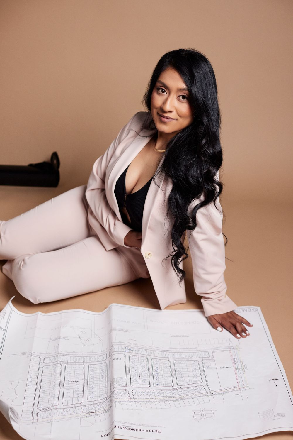 Professional in pink blazer examines architectural drawings on white paper.