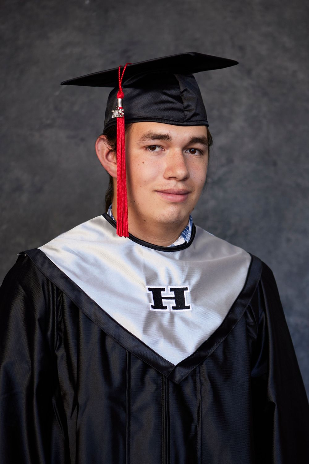 Graduate wearing black cap and gown with white stole and red tassel in professional portrait series.