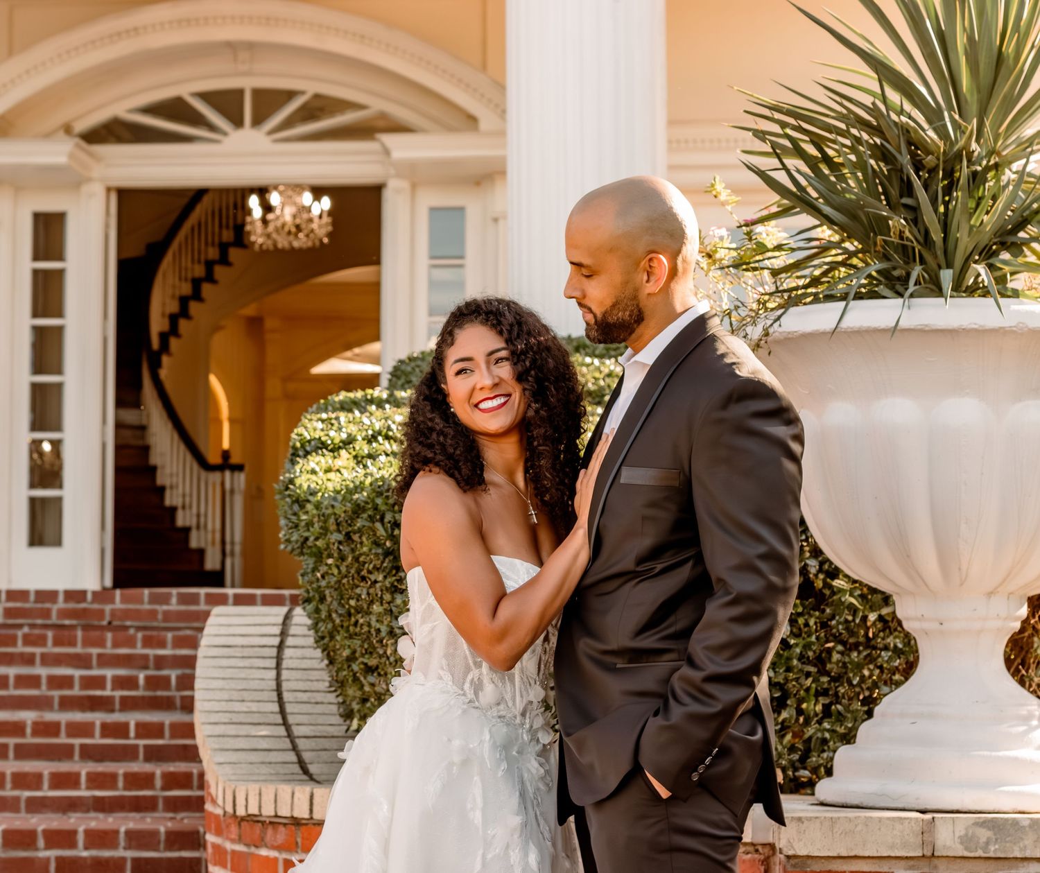 Wedding couple shares intimate moment on grand entrance steps with decorative planters.