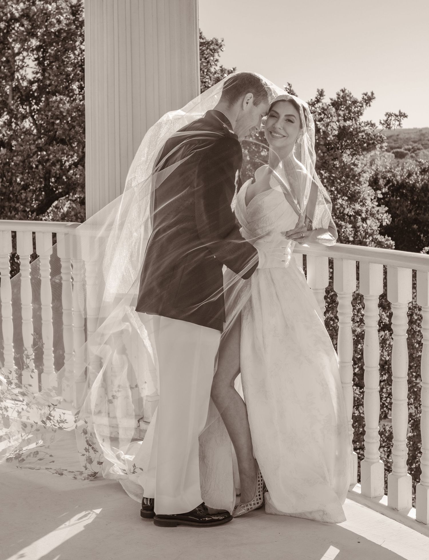 Intimate black and white wedding photo of couple embracing on a columned balcony.