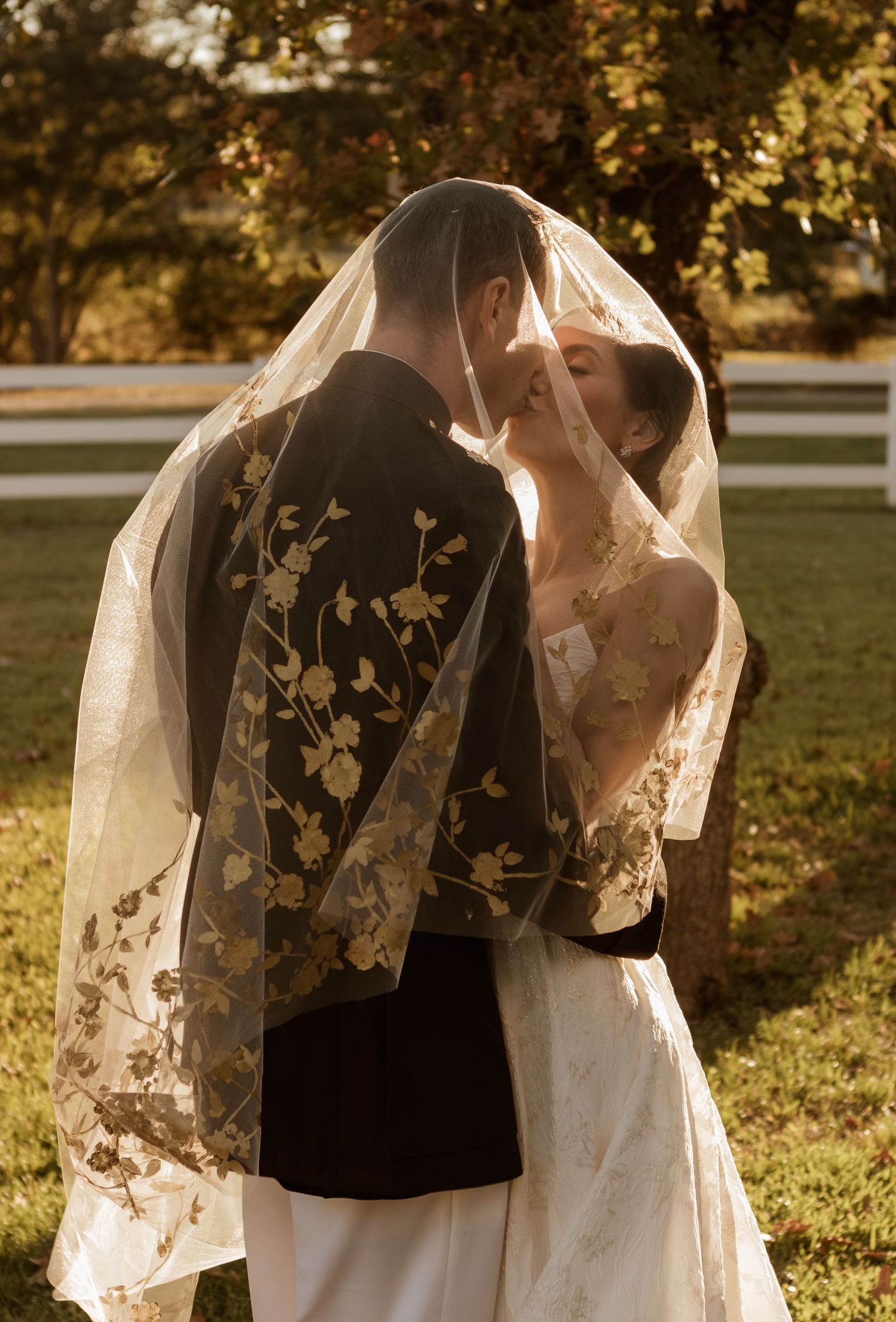 Golden hour wedding portrait with couple sharing intimate moment under decorative veil.