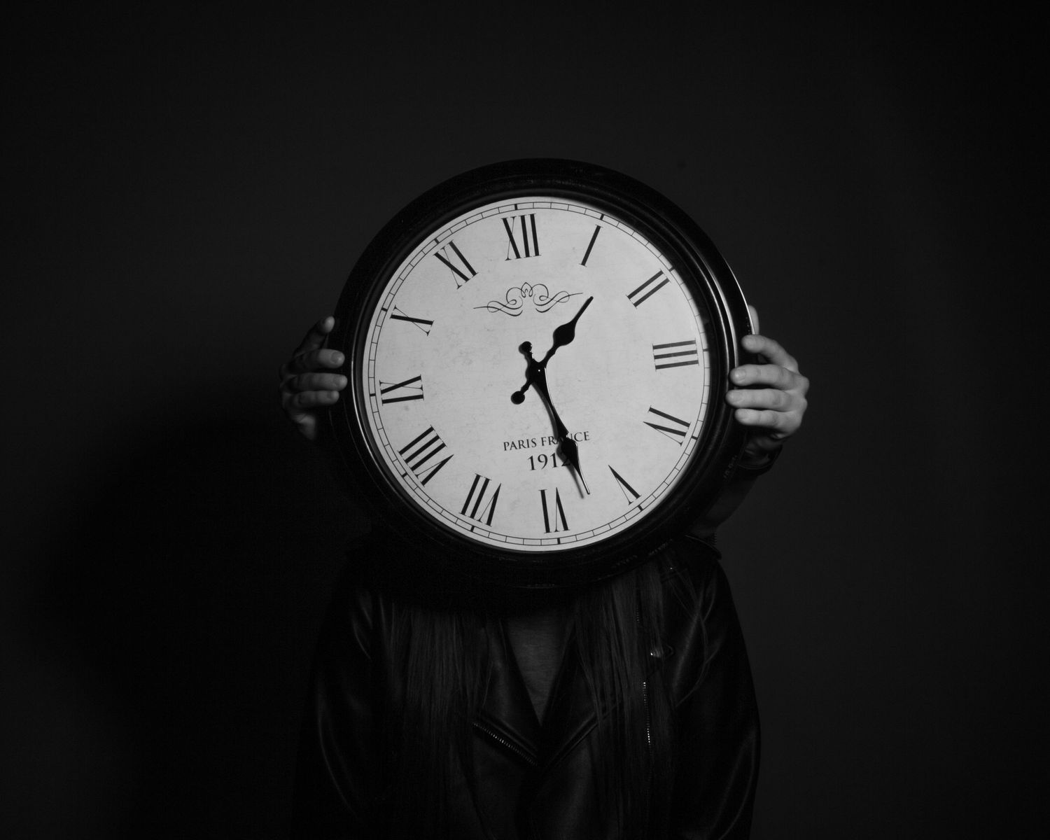 A dramatic black and white composition featuring a classic analog clock face with Roman numerals against a dark background.
