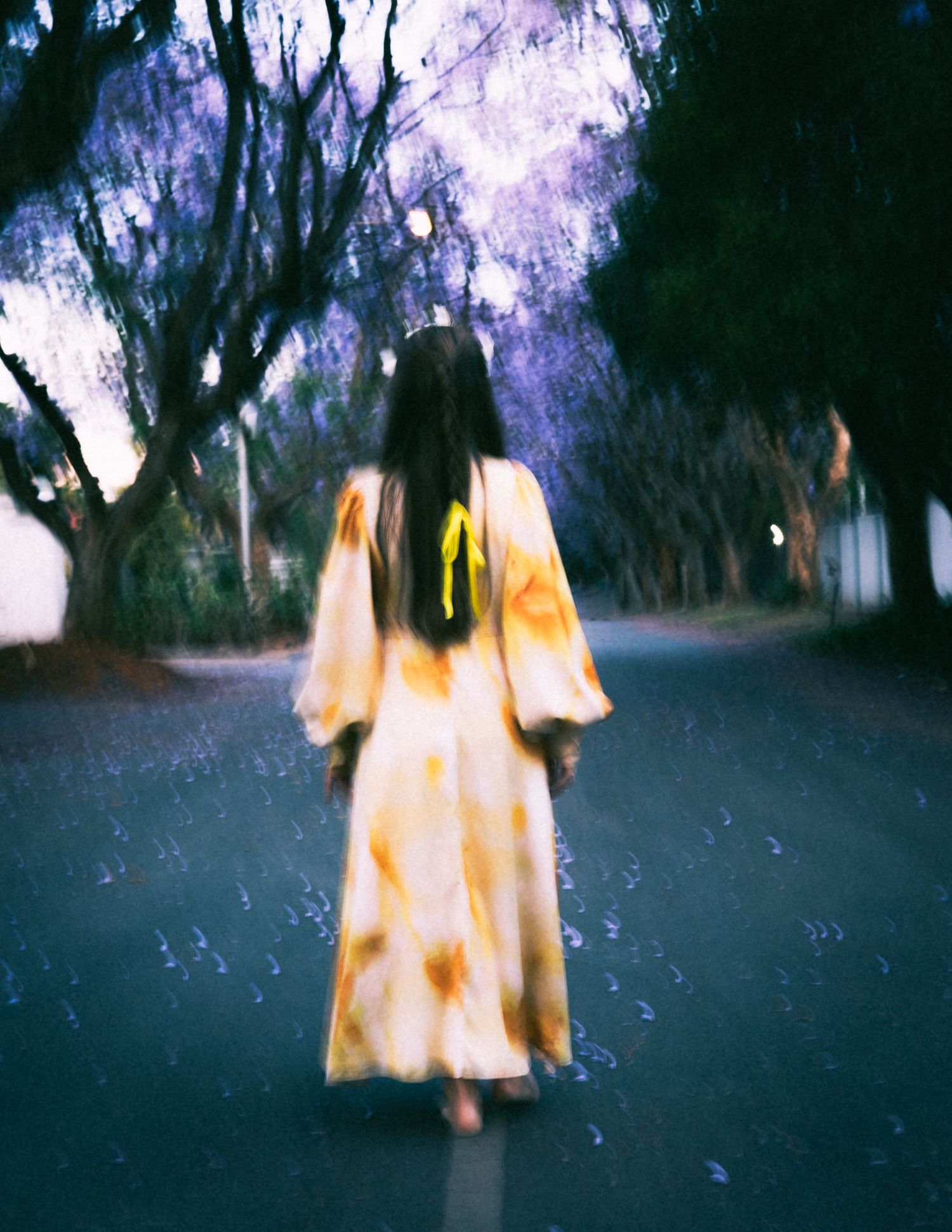 A blurry figure in a yellow dress moves through a dark wooded area creating an ethereal ghostlike effect.