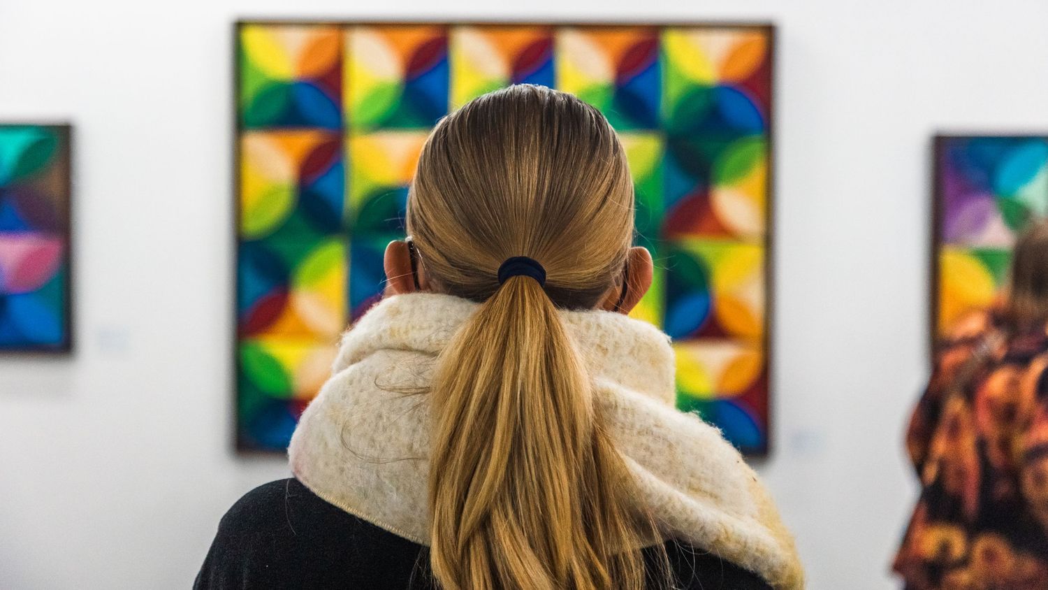 Art gallery visitors viewing contemporary geometric paintings displayed on white walls.
