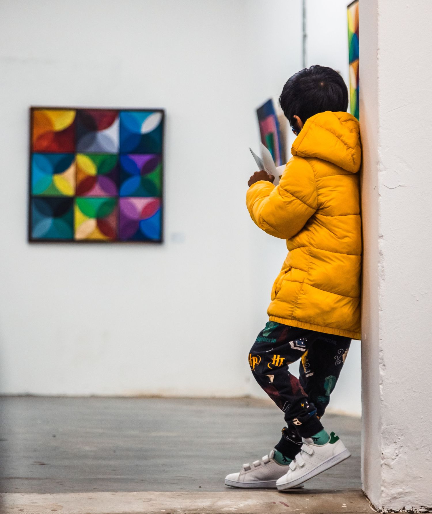 Child in yellow puffer jacket exploring an art gallery featuring geometric artwork.