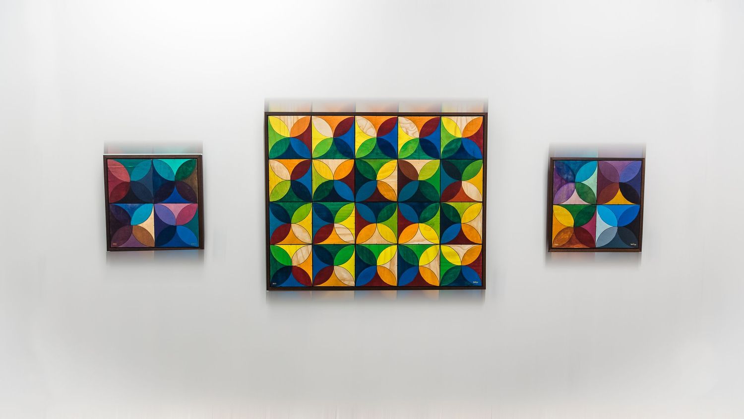 Row of geometric abstract paintings with triangular patterns mounted in a gallery space.