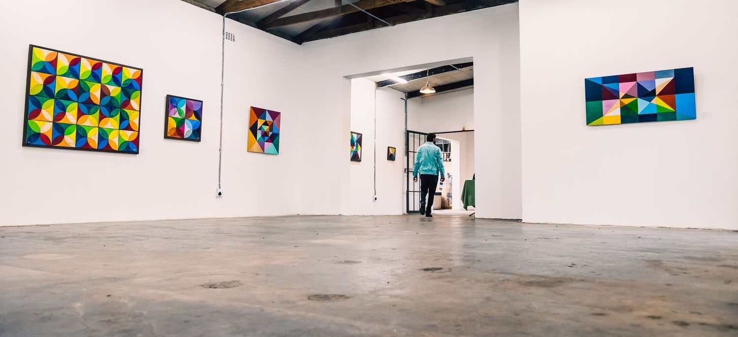 Wide-angle view of a modern gallery space displaying vibrant abstract artworks in a minimalist setting.