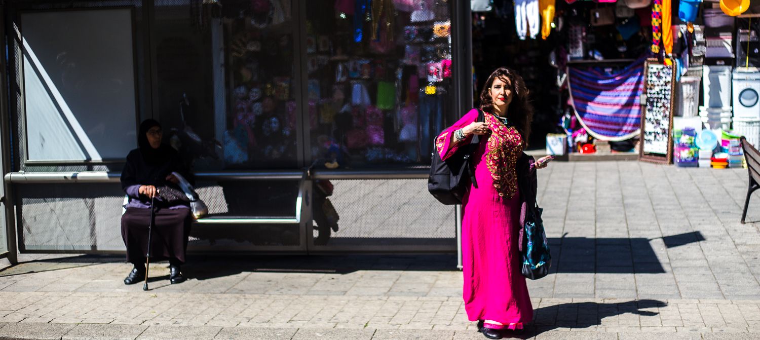 Urban street scene with storefronts and pedestrians in bright daylight.