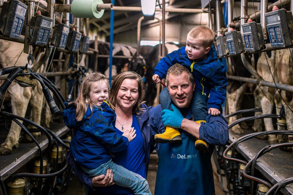 Happy farming family posing together in modern milking parlor with dairy equipment in background.