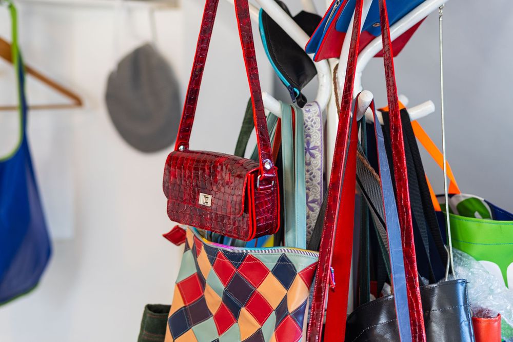 Colorful handbags and purses hanging on hooks against a white wall, featuring a red woven bag and patterned designs.