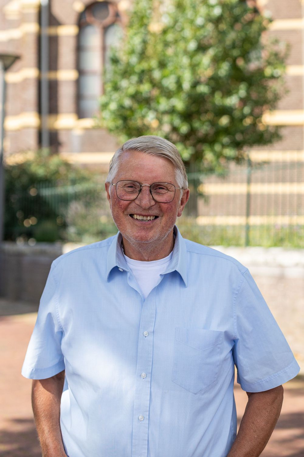 A person in a light blue button-down shirt shown in four similar poses outdoors with trees and buildings in background.