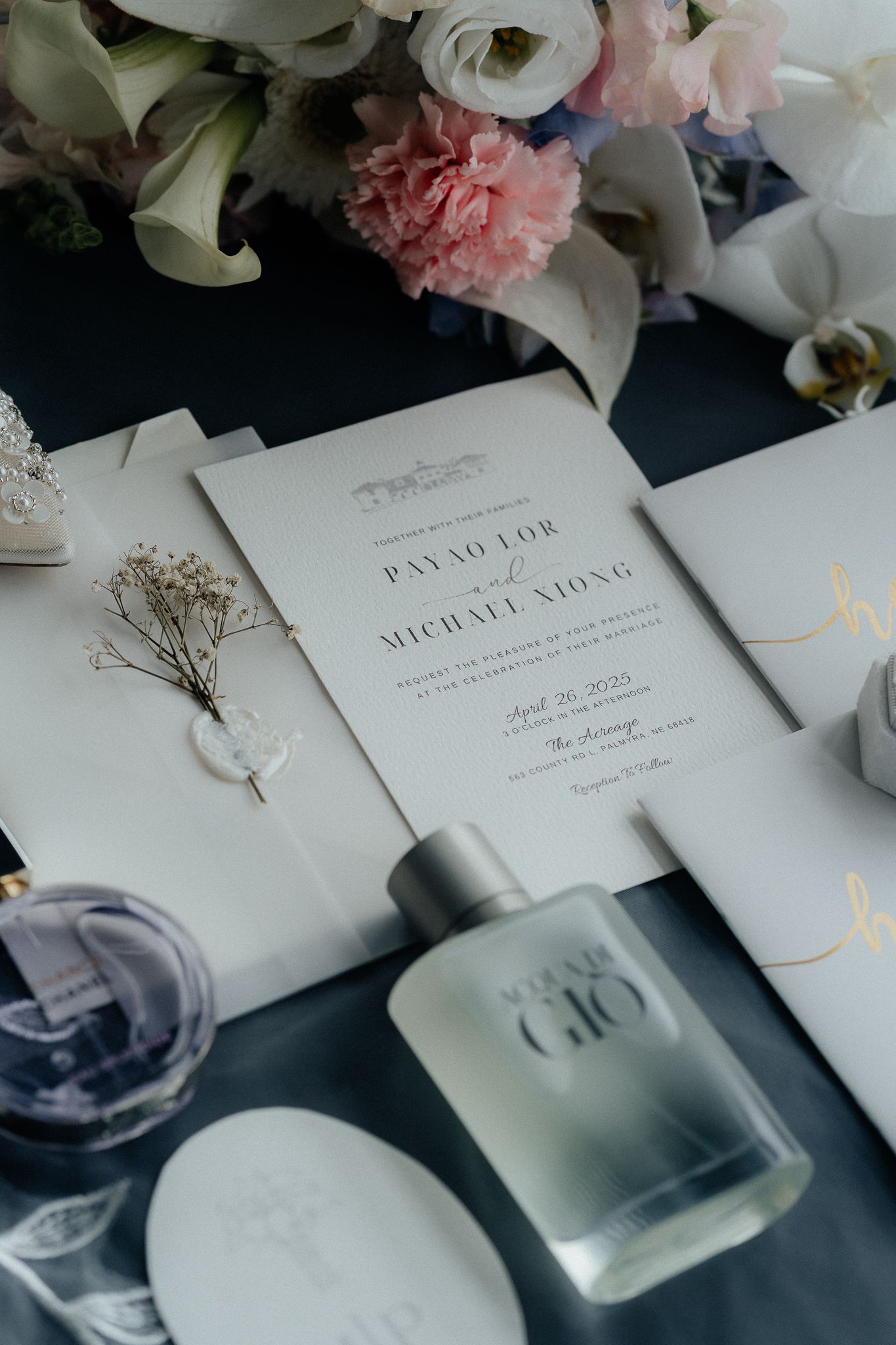 Elegant wedding invitation with floral decorations, perfume bottles and delicate details on dark background.