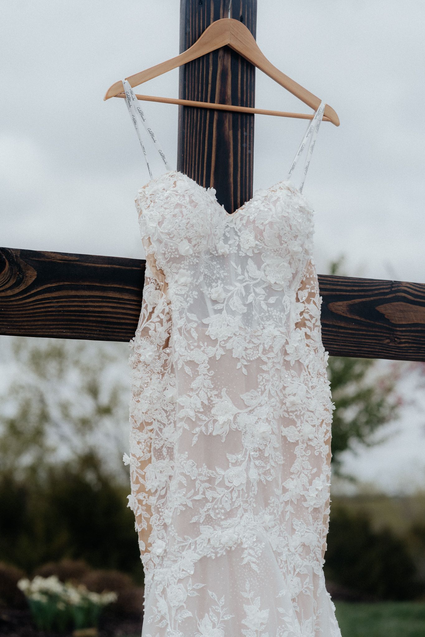 A delicate lace wedding dress with sweetheart neckline hanging on wooden display.