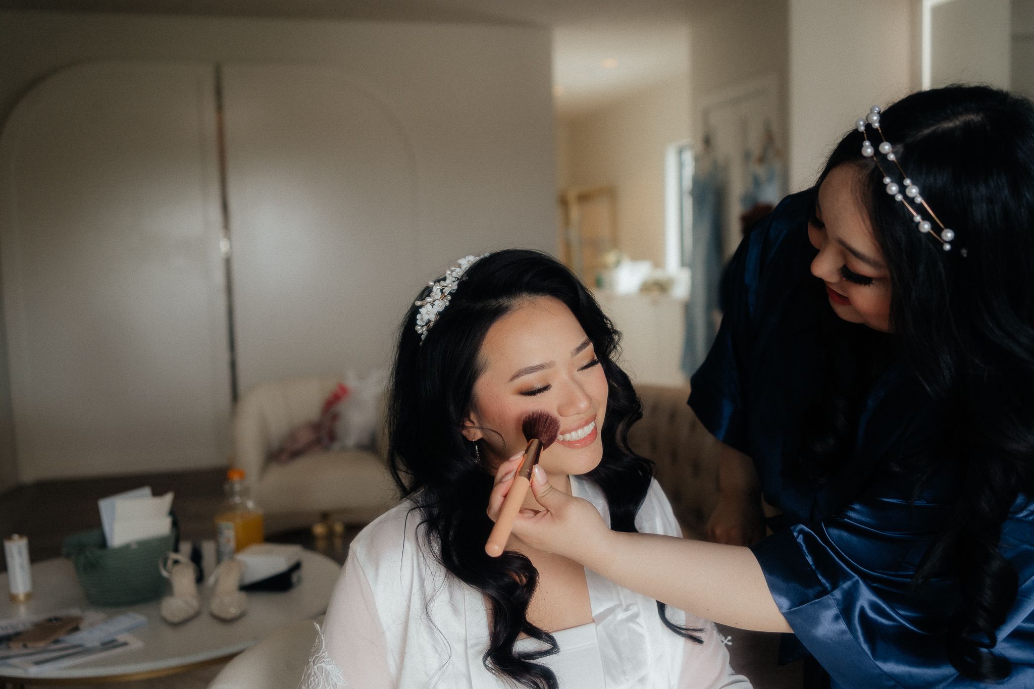 Makeup being applied to smiling bride during wedding day preparations.