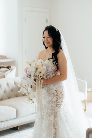 Bride holds elegant white orchid bouquet while wearing lace wedding gown and veil.