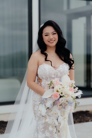A radiant bride in a lace wedding gown holds a beautiful pastel bouquet.