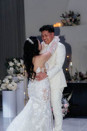 A couple shares their first dance at a wedding reception decorated with elegant white floral arrangements.