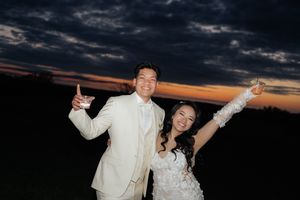 Joyful newlyweds celebrate outdoors against a dramatic sunset sky.