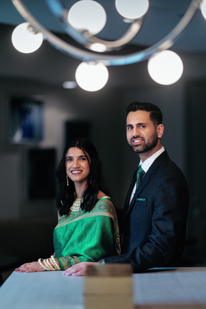 An indian couple from Houston in formal attire sits together at a table, with the woman wearing an elegant emerald green sari.